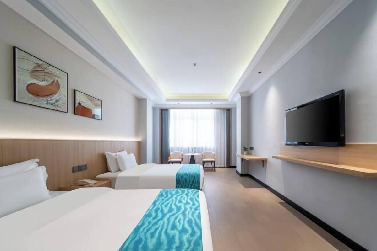 A hotel room with two beds, a TV, a desk, and a window with curtains.