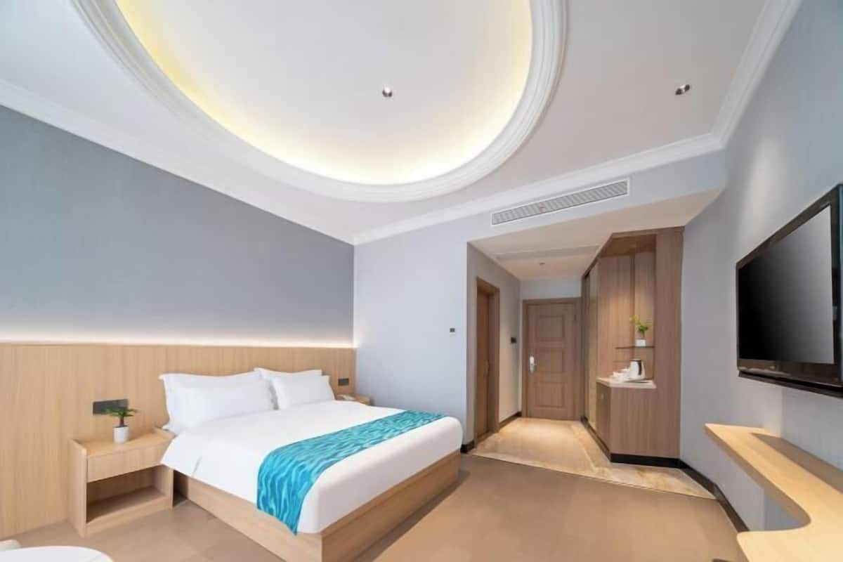A modern hotel room with a large bed, a TV, a desk, and a walk-in closet.