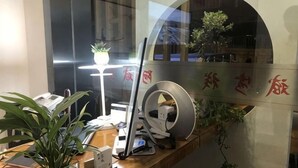 Uma receção com um computador, um telefone, uma lâmpada e uma planta em vaso.