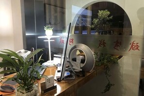 Un mostrador de recepción con una computadora, un teléfono, una lámpara y una planta en maceta.