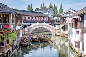 A traditional canal scene with wooden buildings, a stone bridge, and boats. - Abin Inn (Shanghai)