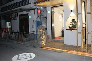 A building entrance with a lion statue, a potted plant, and a red exit sign. - Abin Inn (Shanghai)