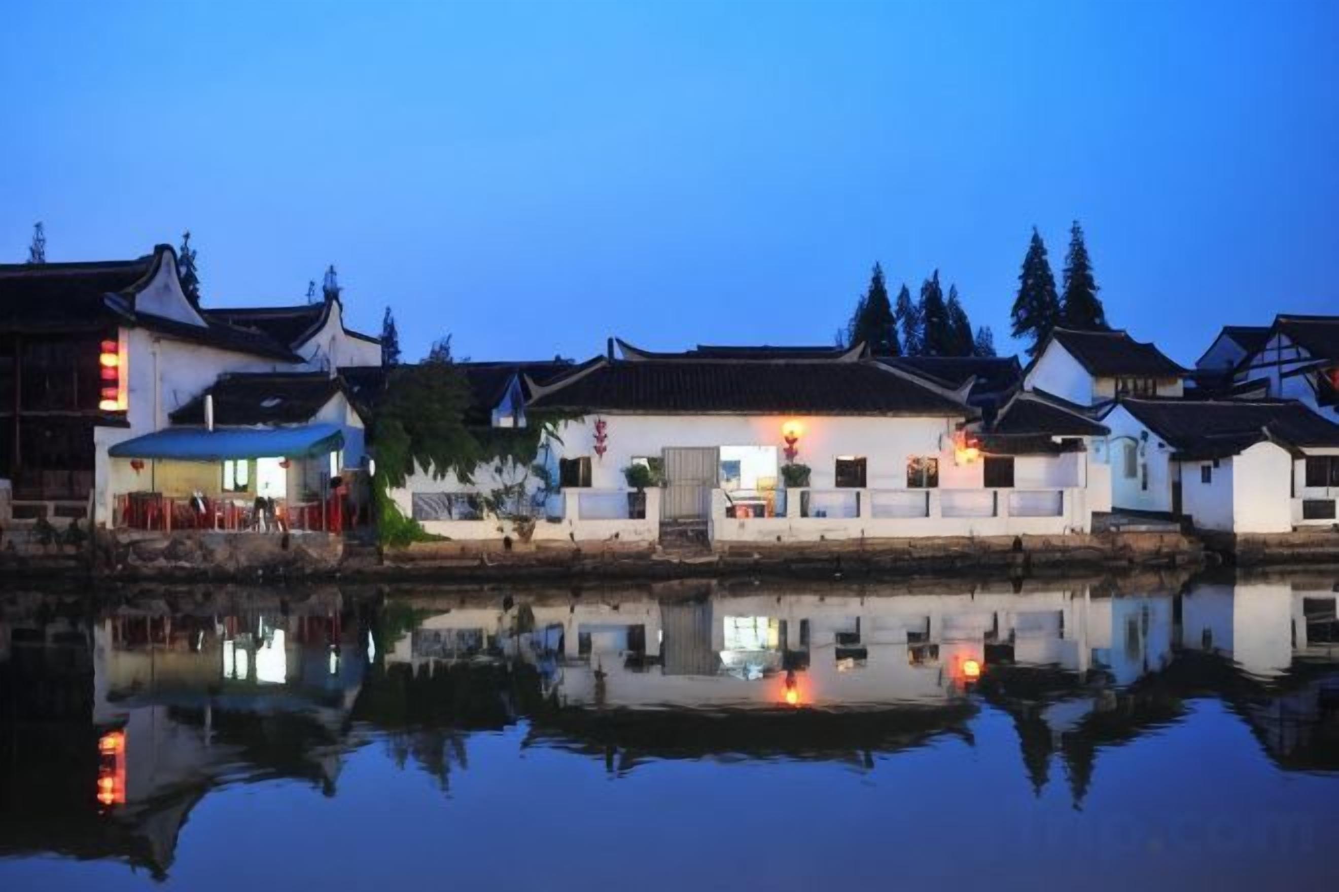 A traditional building with a reflection in the water, a clear sky, and trees in the background.