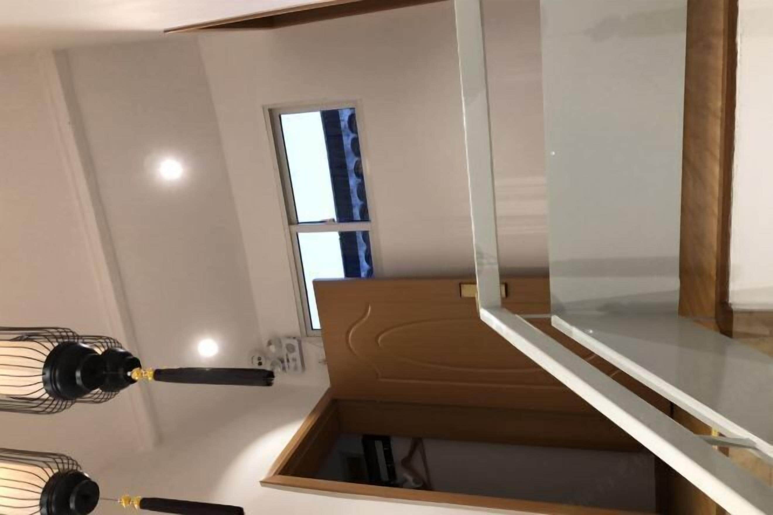 Una habitación con un armario de madera, una ventana con cortina azul y una lámpara en el techo.