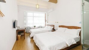 Quarto com duas camas, piso de madeira, televisão e janela com persianas.
