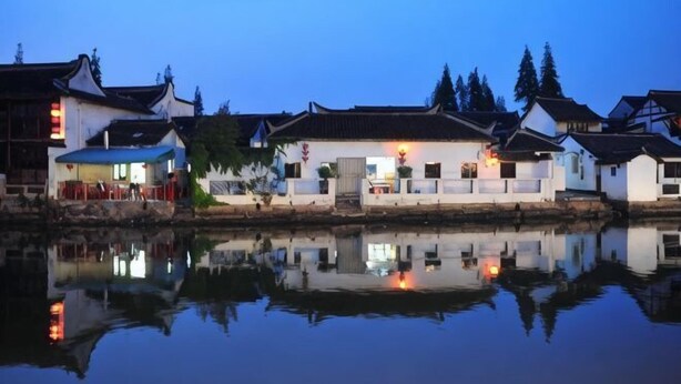 Um edifício tradicional refletido na água, céu claro e ambiente tranquilo.