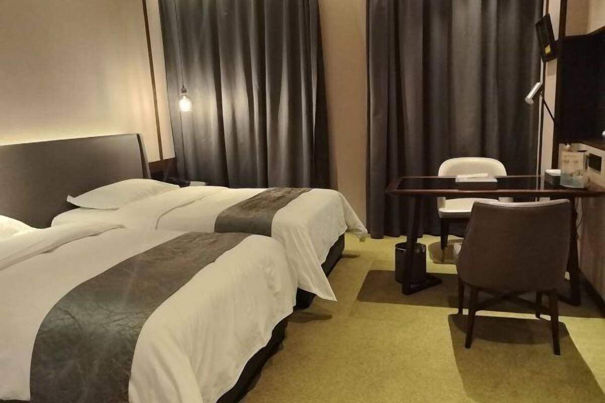 A hotel room with two beds, a desk, a chair, and a TV.