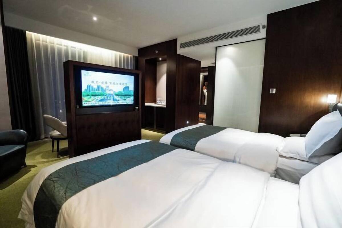 A hotel room with two beds, a TV, a desk, and a chair.