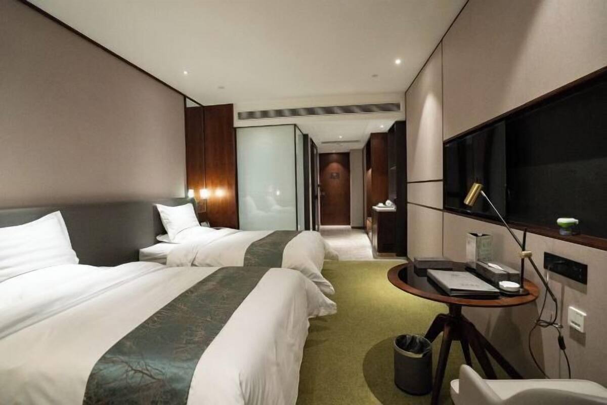 A hotel room with two beds, a desk with a chair, a TV, and a trash bin.