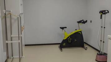 A room with a stationary exercise bike, a standing exercise machine, and a white wall-mounted rack.