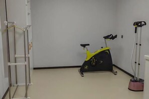 A room with a stationary exercise bike, a standing exercise machine, and a white wall-mounted rack. - Bai Hua Ting International Hotel (Jinan)
