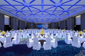 Uma ampla sala de conferências com mesas dispostas em fileiras, carpete estampado e um design de teto azul.