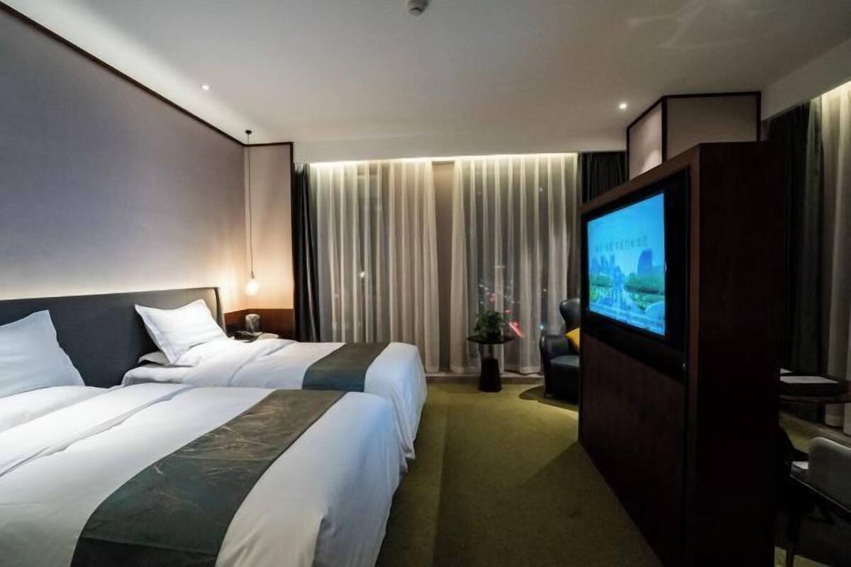 A hotel room with two beds, a television, a desk, and a window with curtains.