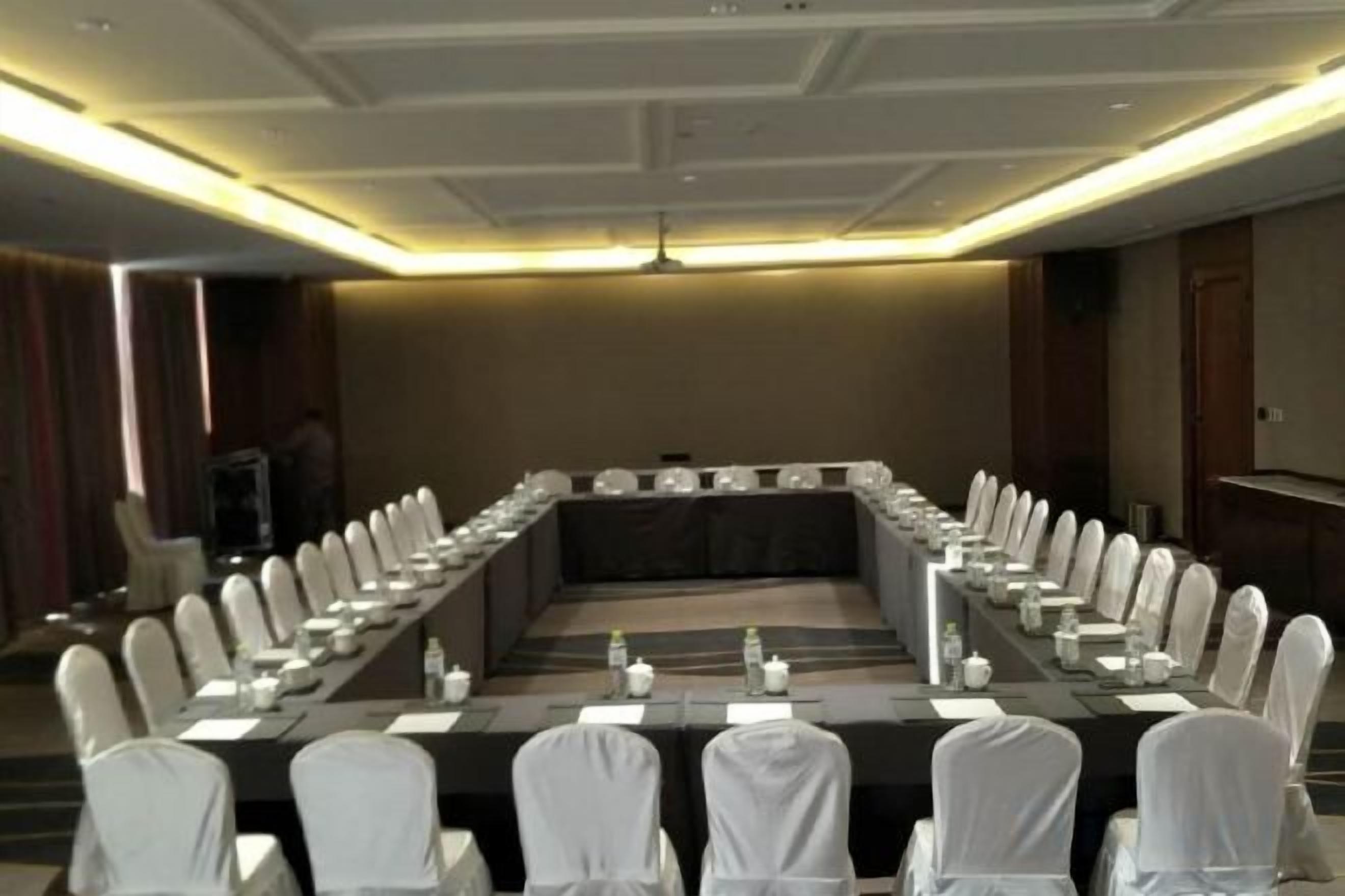 A conference room with a long table, white chairs, and a television screen.
