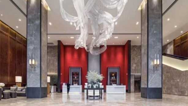 Un vestíbulo moderno con una pared de acento roja, columnas de mármol y una escultura abstracta única suspendida del techo.