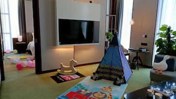 A living room with a flat-screen TV, a play tent, a children's play mat, and a sofa.
