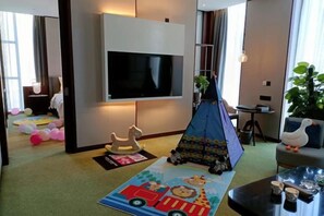 A living room with a flat-screen TV, a play tent, a children's play mat, and a sofa. - Bai Hua Ting International Hotel (Jinan)