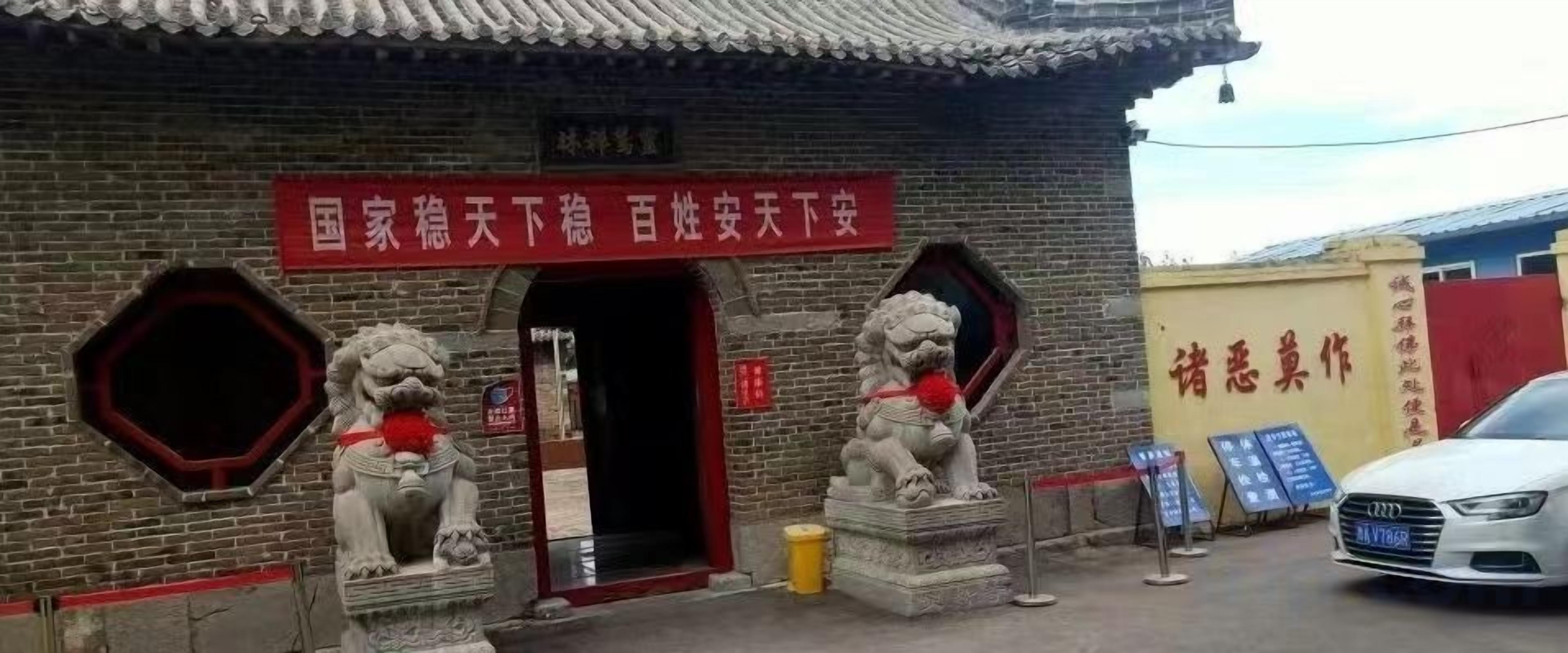 Un edificio de estilo arquitectónico chino tradicional, con un estandarte rojo con texto blanco, dos estatuas de leones en la entrada y un bote de basura amarillo.