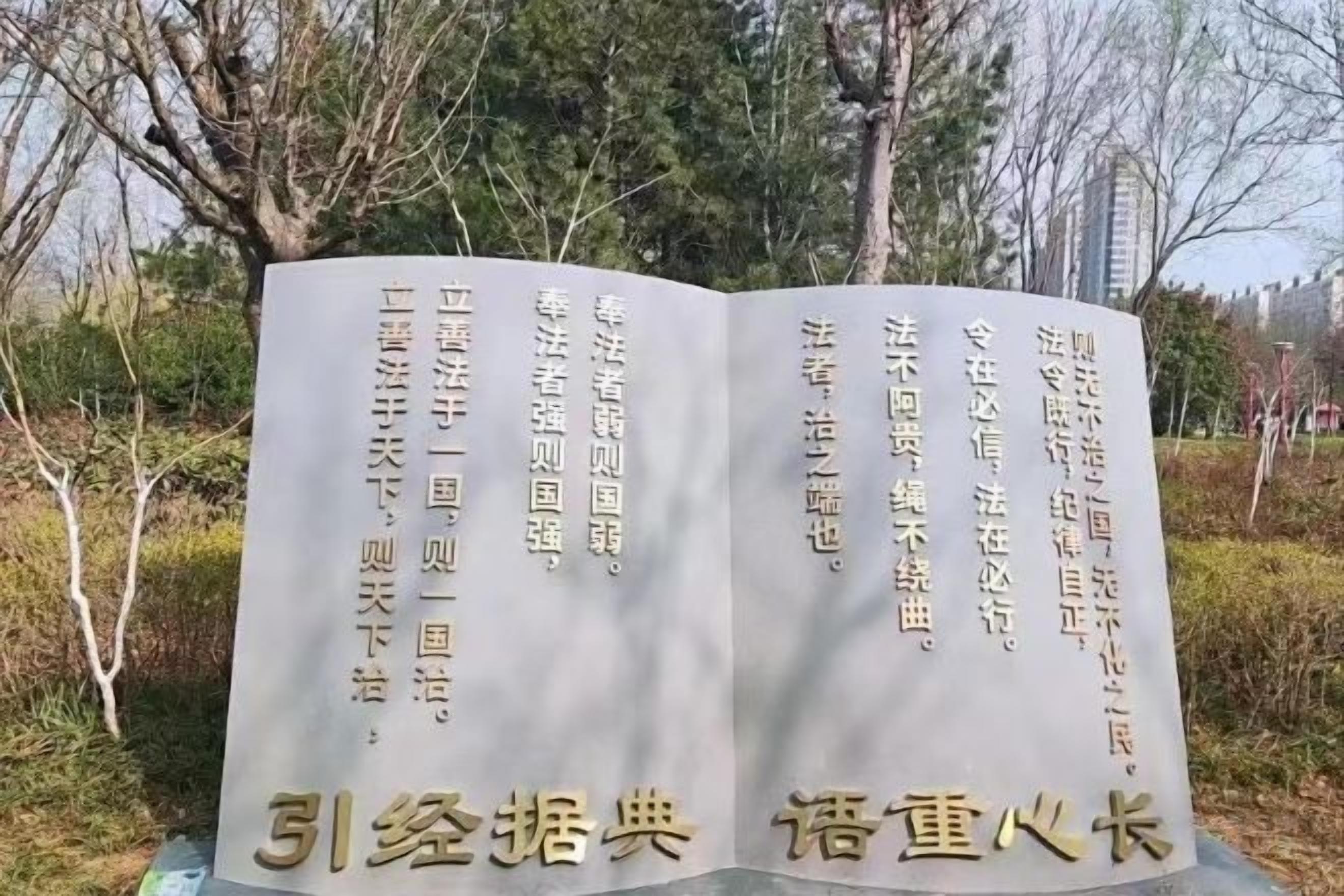 A stone monument with inscriptions, surrounded by trees and shrubs.