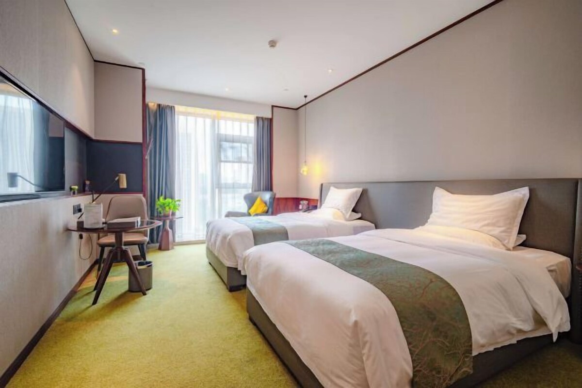 Habitación de hotel con dos camas, un escritorio, una silla y un ventanal grande.