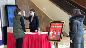 A check-in area with a red table, a digital display, and a poster with health guidelines.