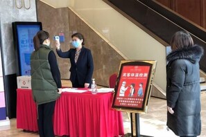 A check-in area with a red table, a digital display, and a poster with health guidelines. - Bai Hua Ting International Hotel (Jinan)