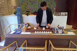 A person preparing tea at a table with teapots, cups, and a tray.