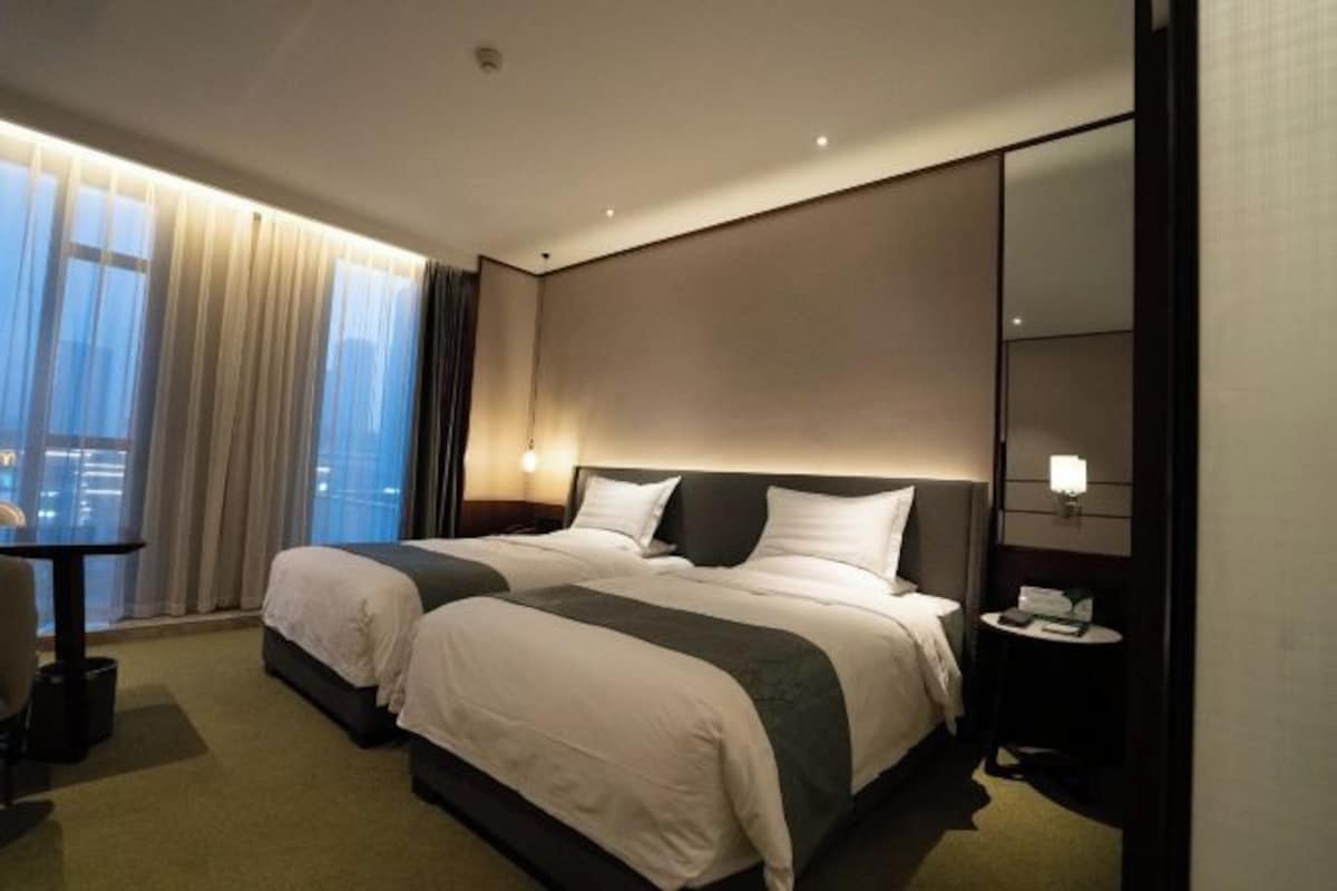 Een hotelkamer met twee bedden, een bureau, een stoel, een nachtkastje en een groot raam met gordijnen.