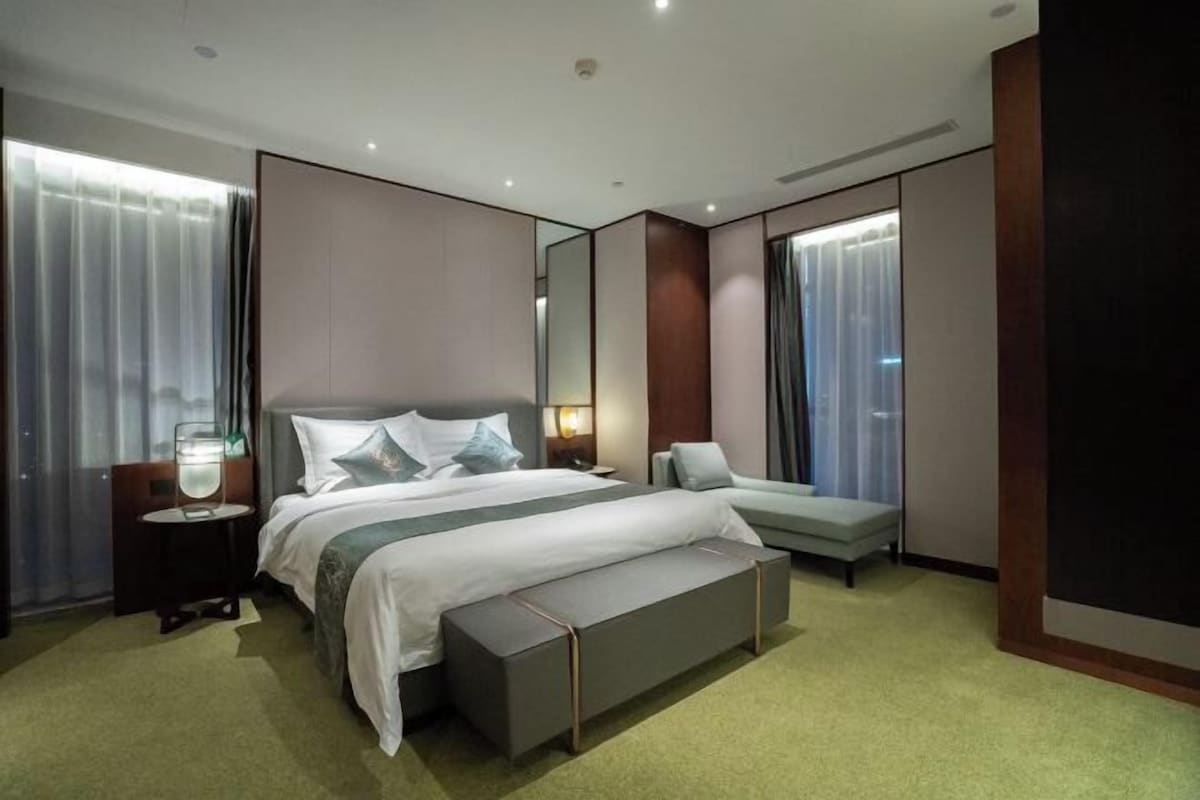 Een moderne hotelkamer met een groot bed, nachtkastjes, een bankje en een grote spiegel.