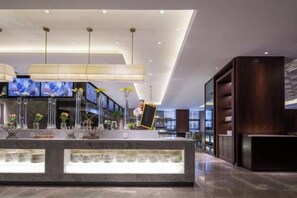 Un hall d’hôtel moderne avec un comptoir d’accueil, de grandes suspensions et un écran de télévision.