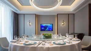 Una mesa redonda dispuesta para una comida, con una pantalla de televisión al fondo.
