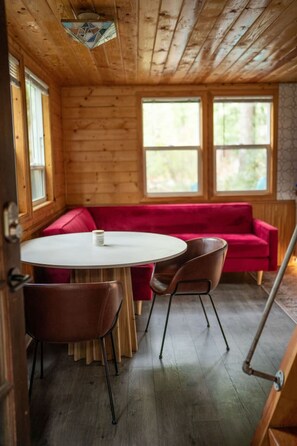 A wooden interior with a round table, red sofa, and two chairs. - Persis River View-Outdoor shower/Sauna/Cold plunge (Sultan)