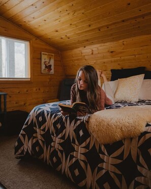 A room with wooden walls, a bed with patterned bedding, a window with blinds, and a small table. - Persis River View-Outdoor shower/Sauna/Cold plunge (Sultan)