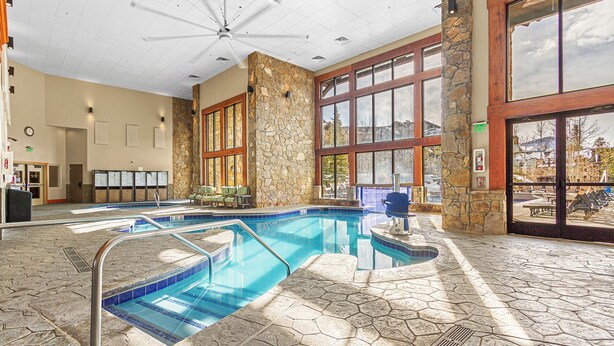 Ein Hallenbad mit Steinwänden und großen Fenstern, einem Deckenventilator und einer Rezeption mit einer Uhr.