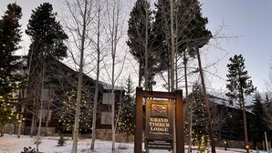 Schild für Grand Timber Lodge, mit Steinunterbau und Holzrahmen, umgeben von Bäumen und Schnee.