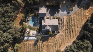 Vista aérea de una casa con piscina, rodeada de árboles y un terreno inclinado.