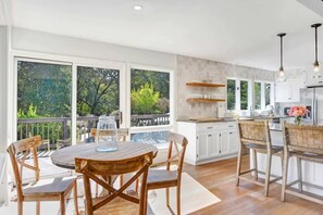 Een moderne keuken met witte kasten, een houten eettafel en een balkon met uitzicht op bomen.