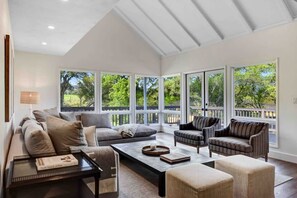 Un salon spacieux avec un plafond haut, de grandes fenêtres et une vue sur la verdure environnante.