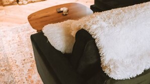 Ein gemütliches Zimmer mit Kamin, einer Couch mit weicher Decke und Holzboden.