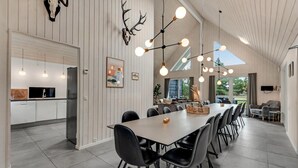 Une cuisine moderne avec des meubles blancs, un réfrigérateur noir et un coin repas comprenant une longue table et des chaises noires.
