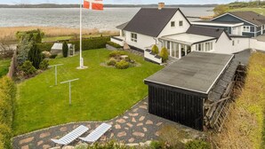 A residential property with a large lawn, a flagpole with a flag, and a view of a lake. - 4 bedroom amazing home in Mariager (Mariager)