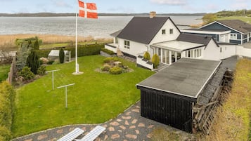 En boligejendom med en stor græsplæne, et flagstang med flag, og udsigt til en sø.
