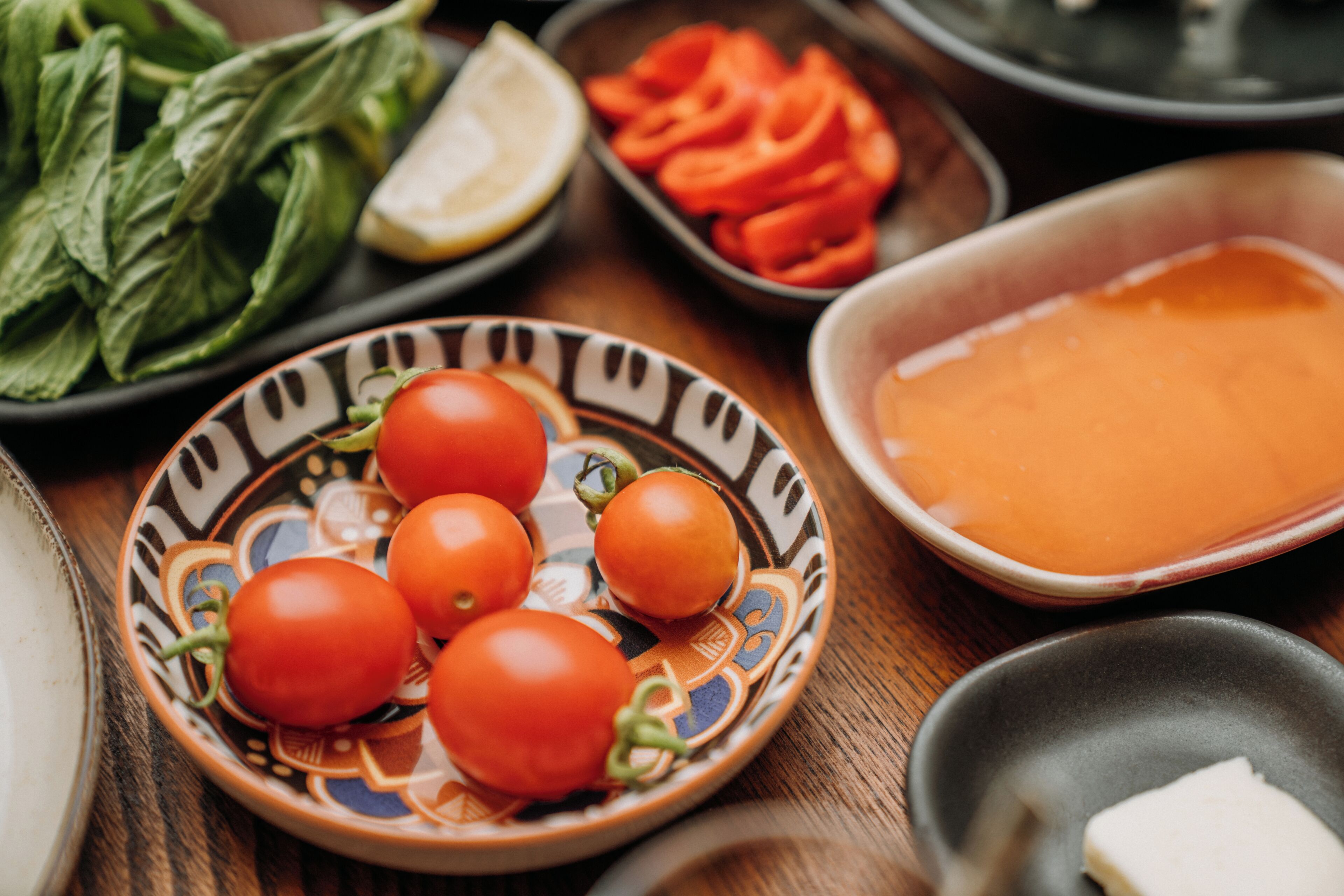 A table with various food items including tomatoes, a bowl of orange sauce, and leafy greens.
