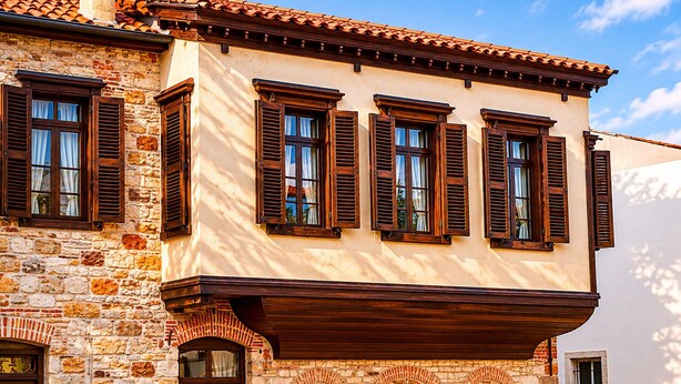 A building with stone walls, wooden shutters, and a tiled roof.