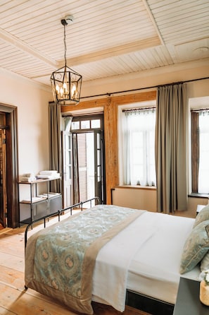 A bedroom with a bed, a hanging light fixture, a window with curtains, and a wooden door. - Nill's Stone House Otel (Cesme)