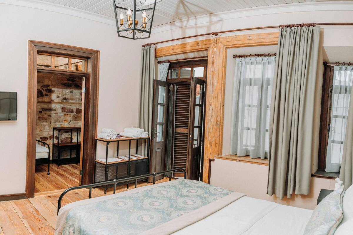 Une chambre à coucher avec un lit, une porte en bois, une fenêtre avec des rideaux, une petite table avec des serviettes et un mur en pierre.