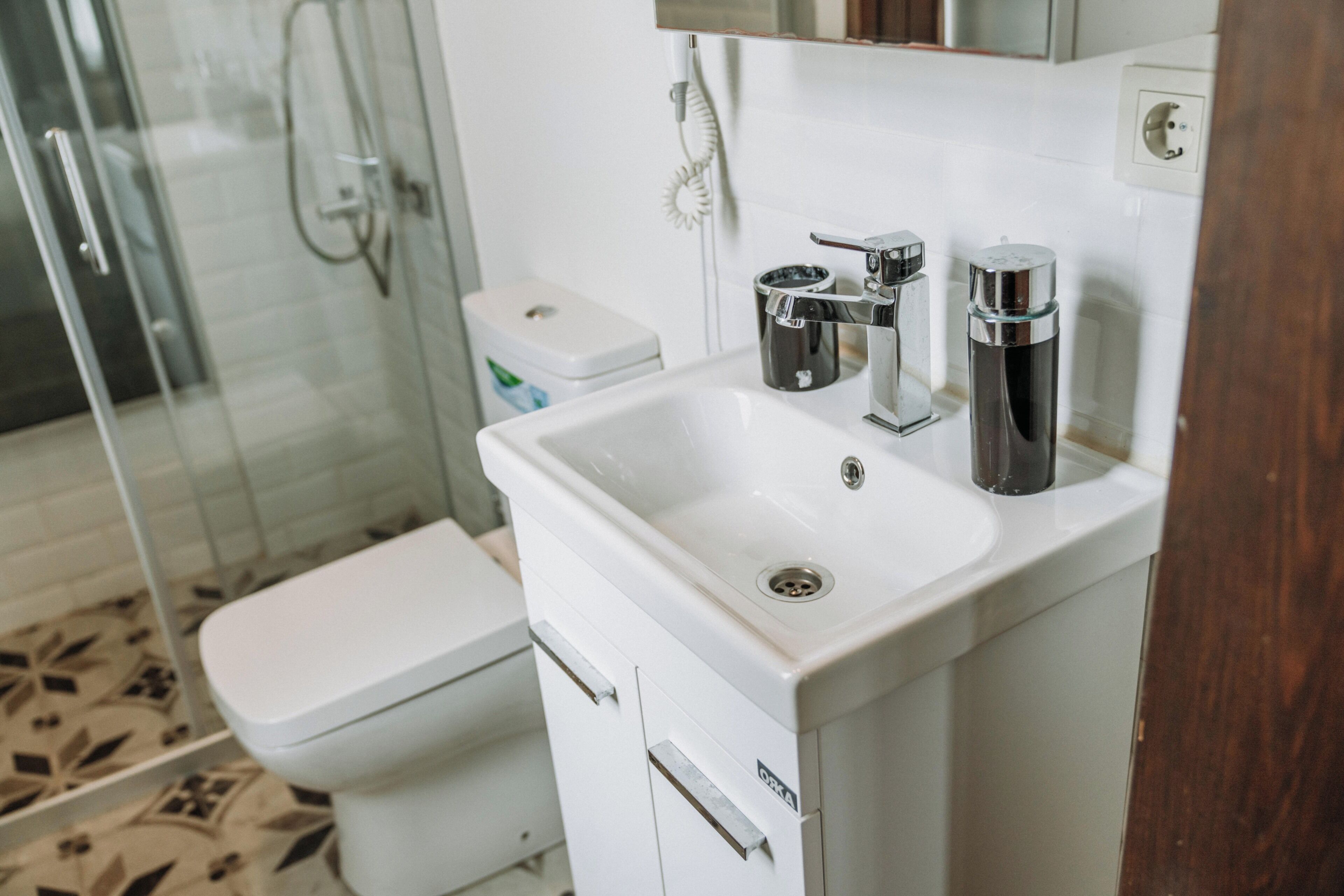 A bathroom with a white sink, chrome fixtures, a toilet, and a glass shower enclosure.