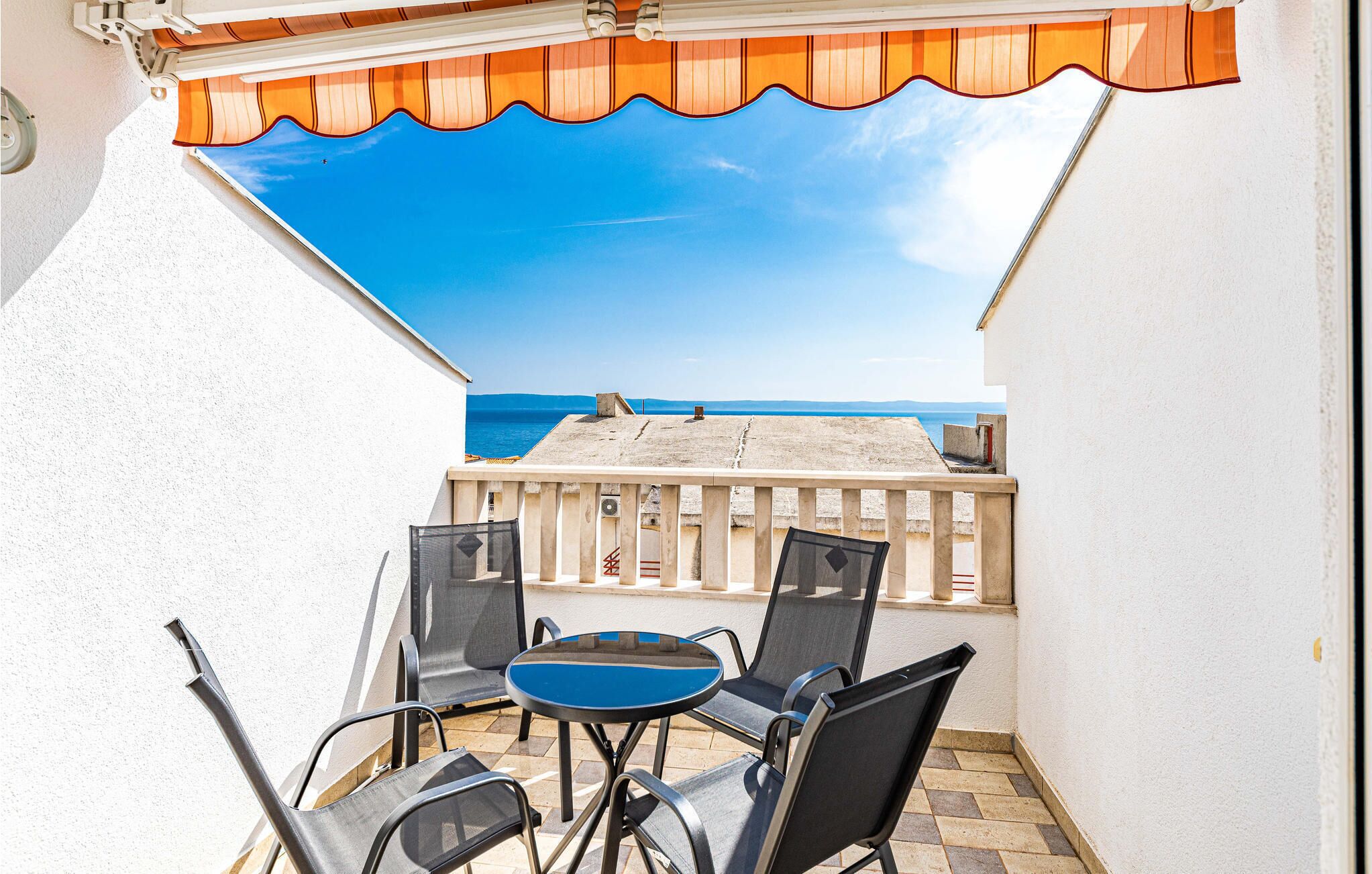A balcony with a view of the sea, a table with chairs, and a railing.