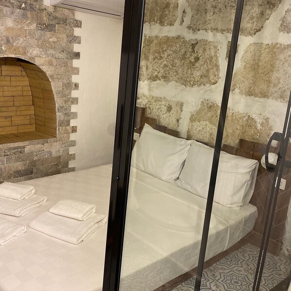 Una habitación con pared de piedra, un banco de madera y una cama con ropa de cama blanca.