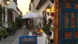 A narrow street with cobblestone pavement, a white umbrella, and a chalkboard sign with text. - Lutfiye Sigacik (Seferihisar)